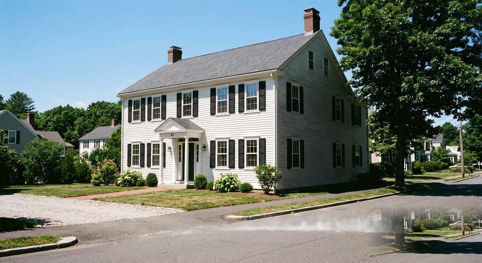 Bright midday sun striking the front of a New England Colonial home, one wall in full sun and the adjacent wall in shade