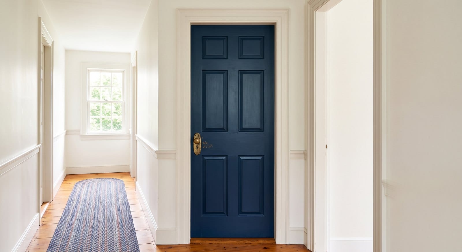 Paneled interior door painted deep navy blue against warm white walls in a MetroWest Boston Colonial hallway