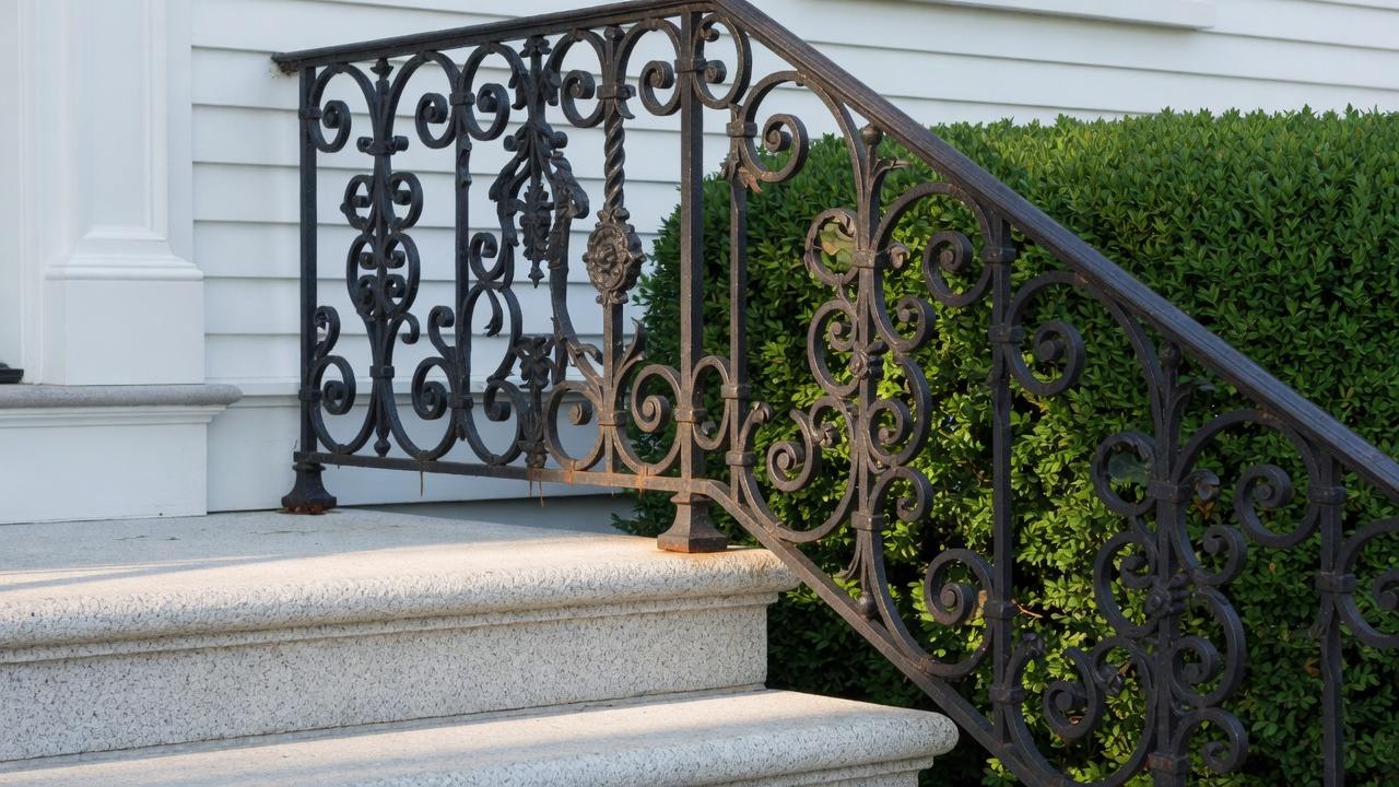 Wrought iron porch railing with rust at weld joints on a MetroWest Boston colonial, early spring light, no people
