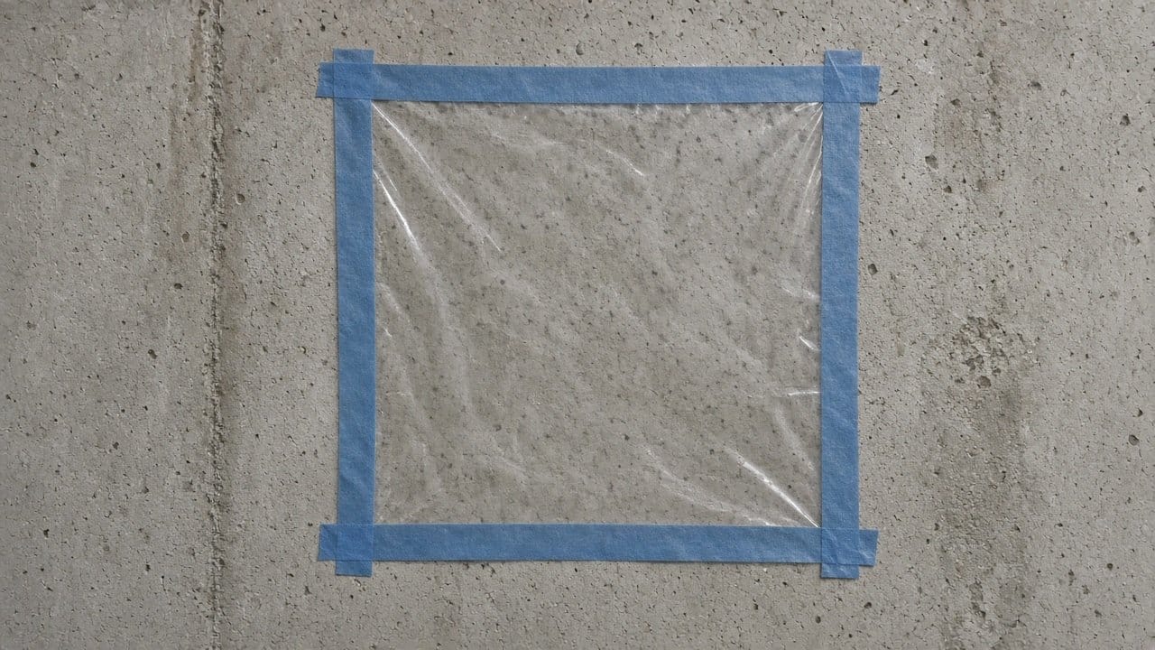 Clear plastic sheet taped to a bare concrete basement wall for a 16-hour ASTM D4263 moisture check